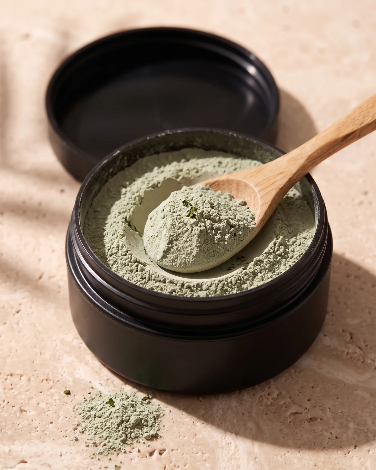 Open jar of Delune Green Tea Clay showing the soft dry sage-green clay powder with a wooden spoon