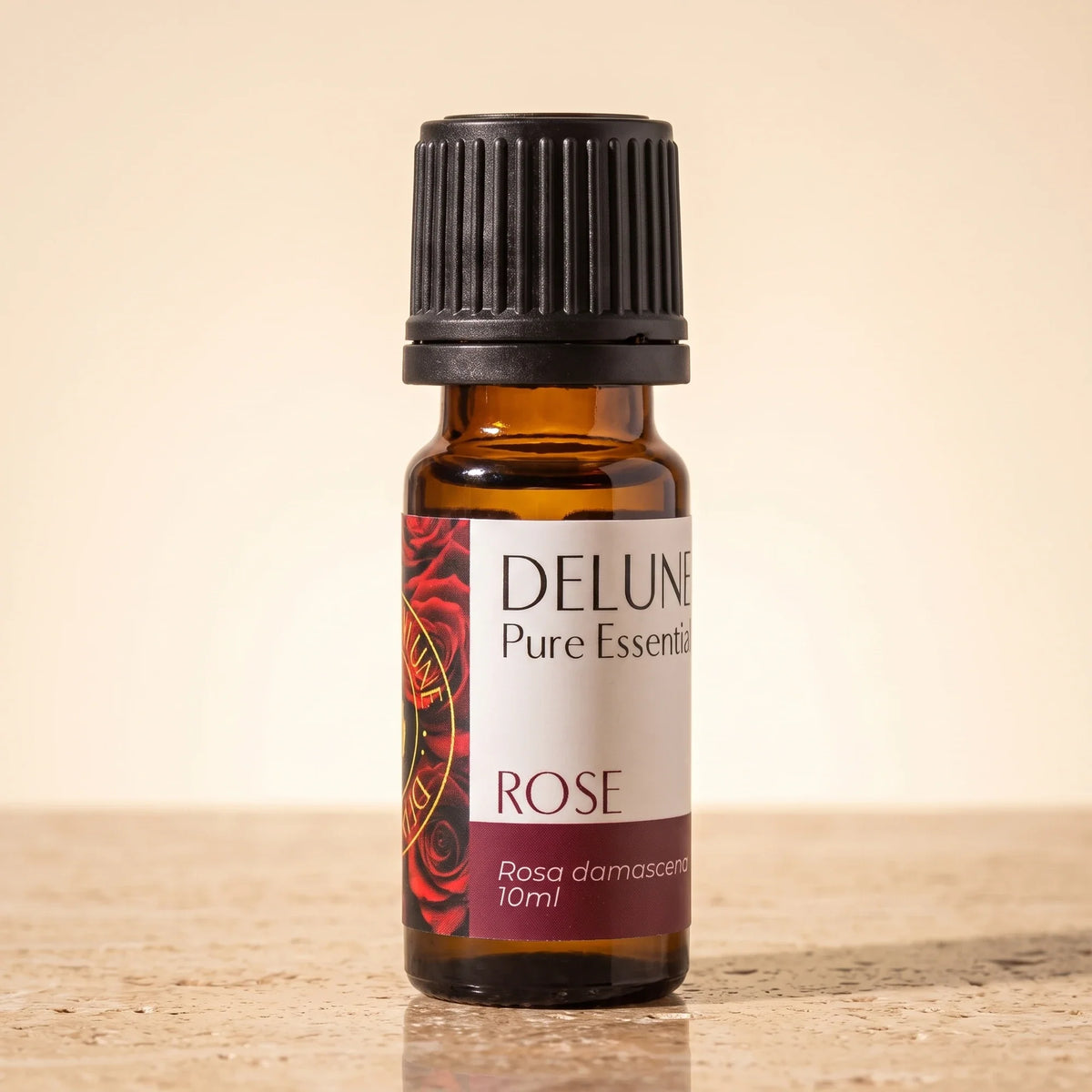 Delune Rose Pure Essential Oil, 10ml amber glass bottle on warm travertine stone