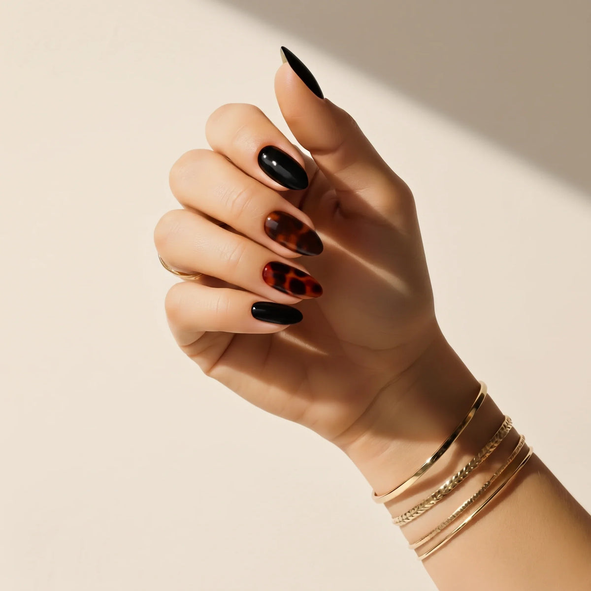 Hand wearing Delune Tortoiseshell Noir nail wraps, black and tortoiseshell nails, against a warm plaster wall
