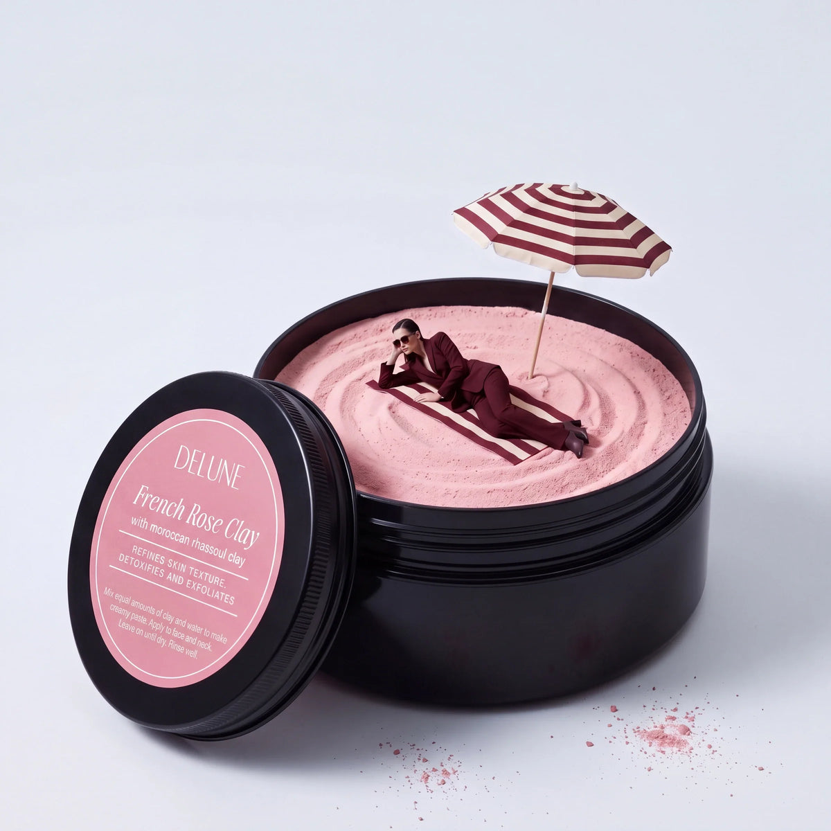 Ritual: a woman in an oxblood suit lounges under a beach umbrella on pink clay inside a giant Delune French Rose Clay jar